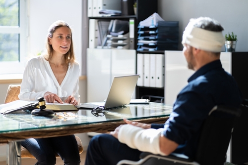 A male patient with head and arm injuries consulting with a female lawyer in a bright office